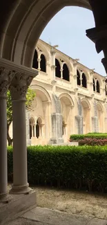 Historic stone cloister view under archway with lush garden.