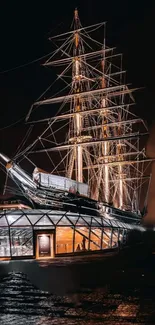 Illuminated historic sailing ship at night on a mobile wallpaper.