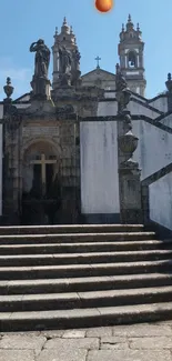 Historic stone staircase with elegant statues and a cross in the background.