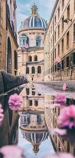 Historic street with dome, flowers reflect in puddle.