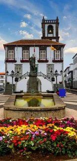 Historic street with fountain and colorful flowers in foreground.