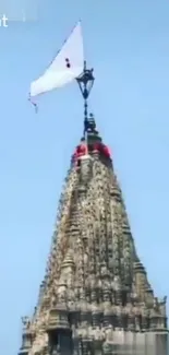 Grand temple spire with a white flag against a clear blue sky.