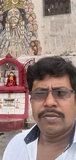 Man posing near intricate temple wall art with cultural and spiritual motifs.