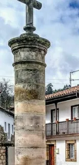 Stone cross in charming village under cloudy sky.