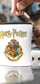 Harry Potter Hogwarts crest mug with hand on white background.