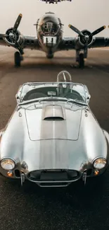 Silver vintage car parked on runway with airplane in background.