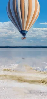 Hot air balloon over calm water with blue skies.