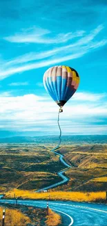 Vibrant hot air balloon over winding road in rural landscape.