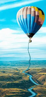 Hot air balloon over winding road under a vibrant blue sky.