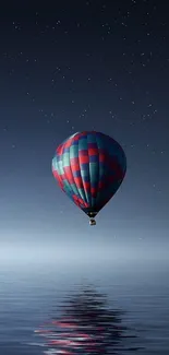 Hot air balloon floats under a starry night sky over calm water.