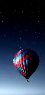 Hot air balloon over calm water at night with stars.