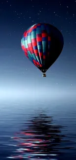 Hot air balloon floats over calm water under a starry night sky.