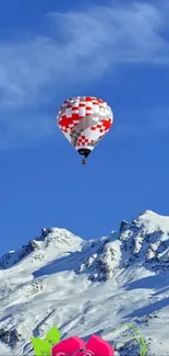 Hot air balloon floating above snowy mountains under a bright blue sky.