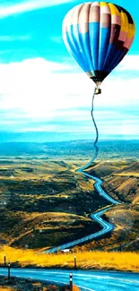 Hot air balloon over winding road in scenic landscape.