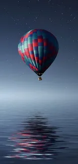 Vibrant hot air balloon floats over calm waters under a starry night sky wallpaper.