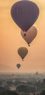 Hot air balloons float over a misty landscape at sunset.