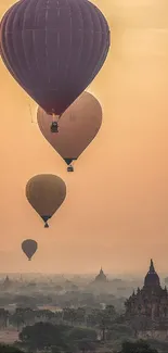 Hot air balloons floating over temples at sunrise with orange sky backdrop.