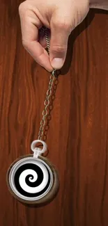 Hand holding a hypnotic spiral on a wood background.