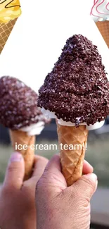 Two hands holding chocolate-dipped ice cream cones with colorful designs.