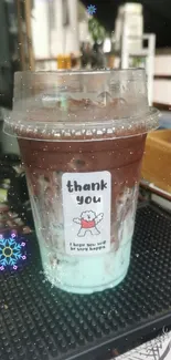 Iced coffee cup with thank you note on a cafe counter.