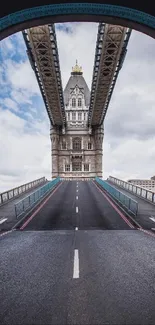 Tower Bridge seen through arch with road leading to it under cloudy skies.