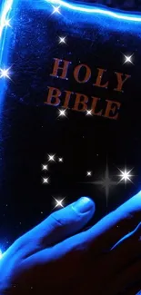 Glowing blue Holy Bible with stars illuminating a hand holding it.