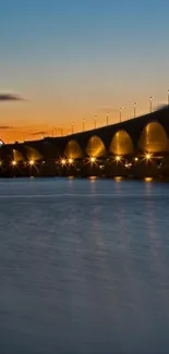 Illuminated bridge over water at sunset.