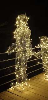 Two illuminated human-shaped sculptures with fairy lights on a night pier.