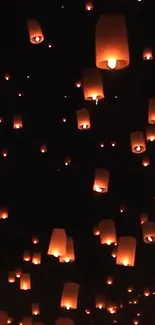 Floating lanterns illuminate a dark sky with a warm glow, creating a serene scene.