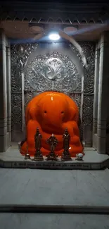 Orange Ganesh idol in a detailed temple setting, beautifully illuminated.