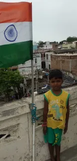 Young boy standing by the Indian flag on a rooftop, showcasing cultural pride.