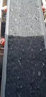 Conveyor belt with dark stones on industrial background.