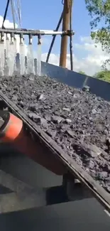 Gray conveyor belt with rocks and machinery in action.