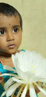 A child holding a white flower, looking away in a serene setting.