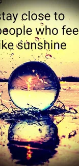 Glass sphere on reflective surface with sunshine and inspirational quote.