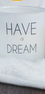 White candle with 'Have a Dream' text on soft blanket.