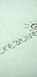 Handwriting "Be Creative" with light bulb drawing on paper.