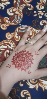 Hand with henna design against vibrant patterned background.