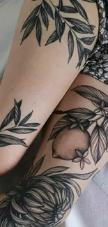 Detailed black ink tattoos on skin featuring botanical designs.