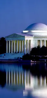 Jefferson Memorial at night with reflection in calm water under blue sky.