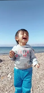 Child laughing on a sunny beach with blue sky and ocean backdrop.