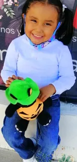 Smiling child holding a plush green frog toy.