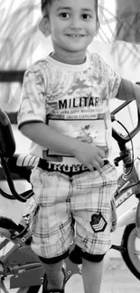 Black and white image of a joyful child with a bicycle, smiling brightly.