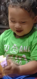 A happy child in a green shirt smiling and playing joyfully with a toy.