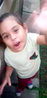 Cheerful child waving with a joyful smile in an outdoor setting.