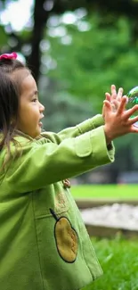 Young child in green coat reaching for a bubble outdoors.