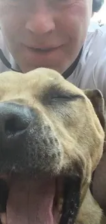 A man takes a joyful selfie with his yawning, happy dog outdoors.