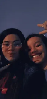 Two friends sharing a joyful selfie at dusk with a dark blue sky.