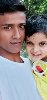 Father holding daughter, smiling outdoors.