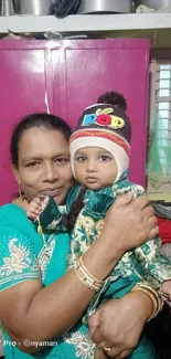 Mother holding baby in colorful attire, smiling indoors.